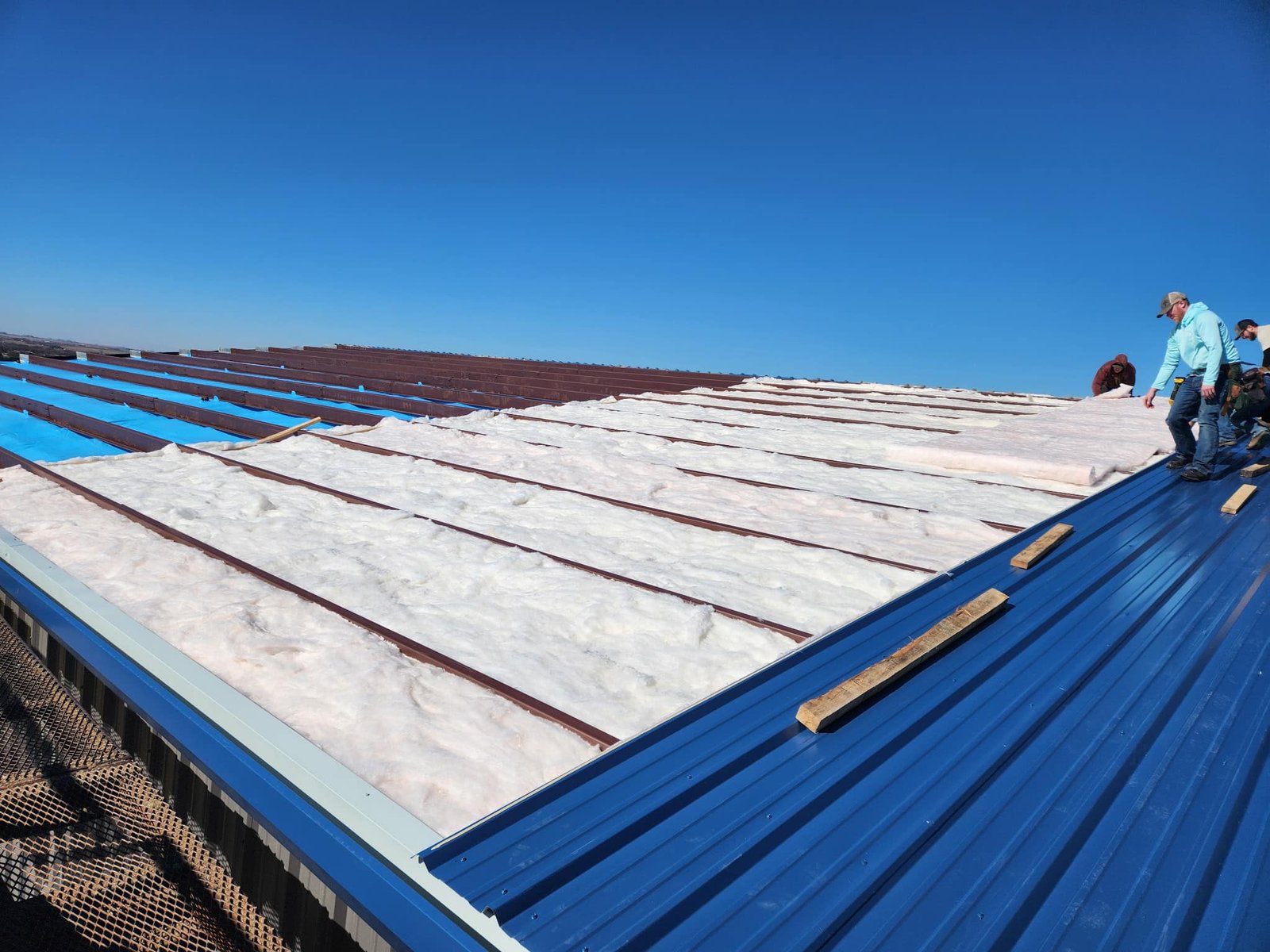 Metal frame commercial building undergoing insulation installation on its exterior structure.