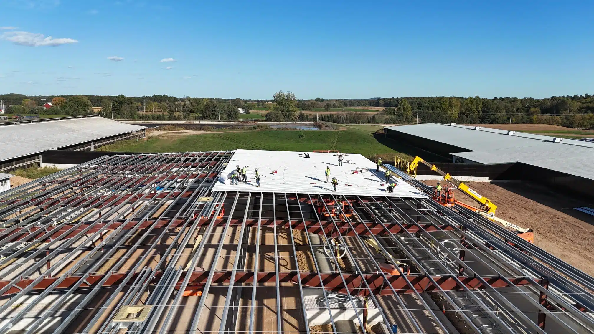 Drone view of metal commercial building under construction with roof insulation installation in progress.