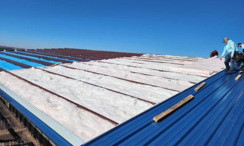 Metal frame commercial building undergoing insulation installation on its exterior structure.
